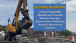 Excavadora limpiando escombros con trabajadores en equipo protector.