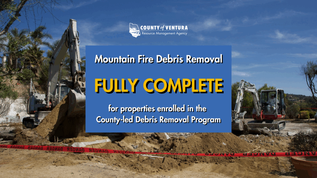 Excavators at a debris removal site with a sign that reads "Mountain Fire Debris Removal Fully Complete."