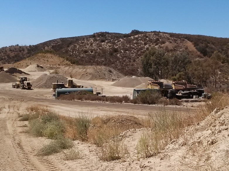 Excavation site with heavy machinery and dirt piles in a hilly landscape.