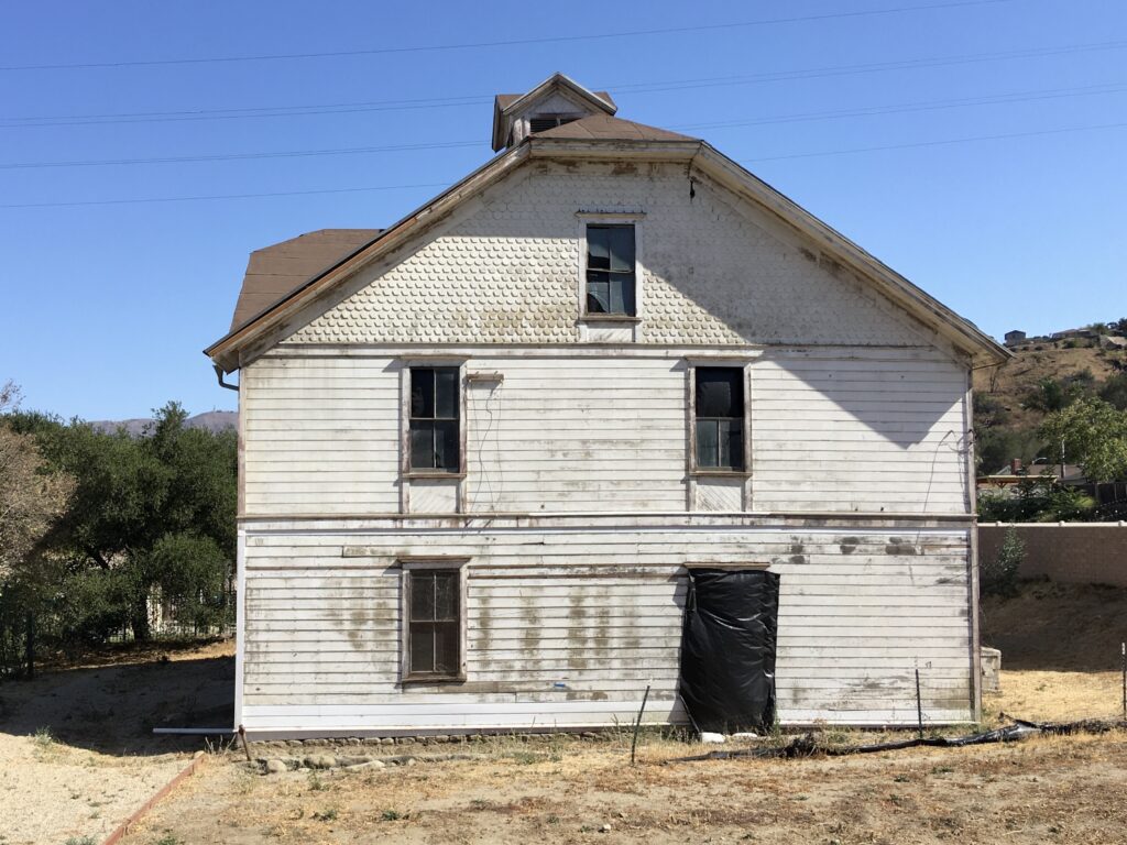 Front view of an old white barn with peeling paint, black tarp on lower part. Credit: Craig Baker, 2021.