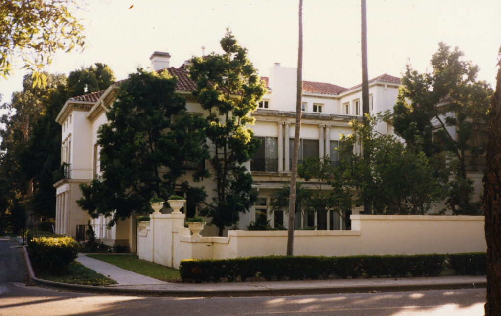 Side view of Thomas R. Bard Mansion, featuring white walls, lush greenery, and tall palm trees.