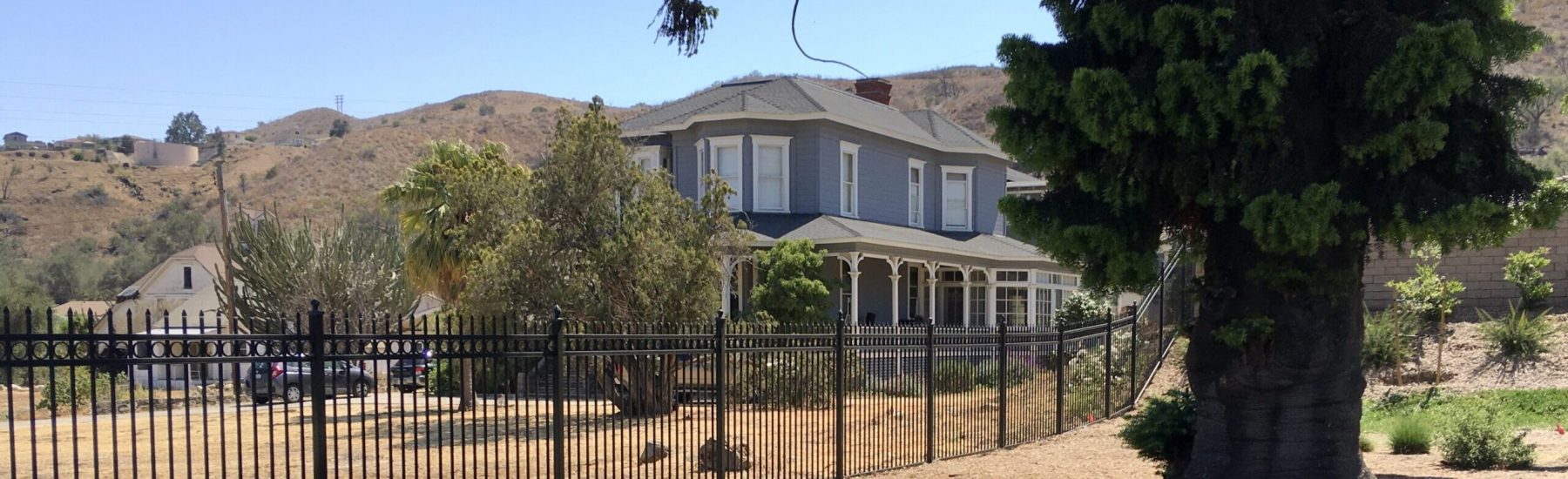 A historic house with a fenced yard, surrounded by hills, and a plaque in the foreground. Hardison House, 2021. Credit: Craig Baker.